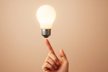 Poster - Glowing light bulb balanced on a finger against beige background symbolizing creativity and innovation in business and abstract thinking concept.