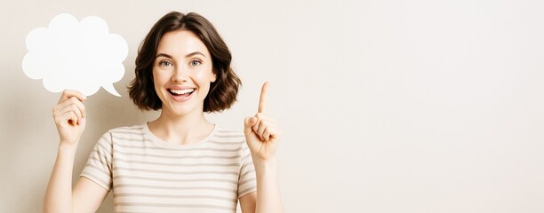 Poster - Smiling woman holding blank speech bubble and pointing up against light background with copyspace for text or design, perfect for creative mockup..