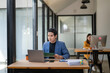 © Apichat - A man is sitting at a desk with a laptop and a stack of papers