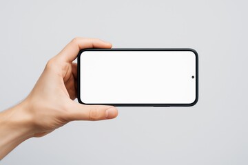 Poster - Hand holding smartphone with blank white screen in horizontal position on light background for clean display mockup or poster design template concept.