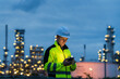 © VStudio - Industrial worker using a smartphone for communication at an oil and gas plant at night.