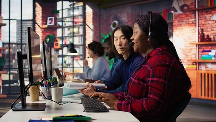 Poster - Experienced call center team leader assisting employee and drinking coffee in office. Asian account manager doing teamwork with colleague, enjoying beverage in workplace, camera B