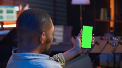 Poster - African american young adult laying on the sofa with mockup screen, feeling happy and relaxed with flexible work schedule at home. Freelancer uses phone relaxing in the living room. Camera B.
