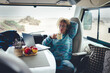 © simona - Modern woman working remotely from inside a stylish camper van, using laptop and smartphone while traveling full-time. Digital nomad lifestyle combining freedom, technology, mobility and remote work