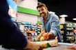 © Drazen - Happy man putting groceries on checkout counter while buying in supermarket.