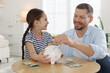 © New Africa - Father and daughter putting pocket money into piggybank at table indoors