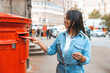 © Iryna - Woman mailing a letter during a sunny day in an urban area surrounded by colorful postal boxes and busy streets
