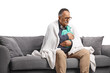 © Ljupco Smokovski - Ill mature man wrapped in blanket sitting on a sofa and holding a body warmer