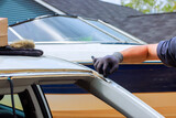 Worker works on car in driveway, repairing vehicle while auto sits nearby under replacement damaged windshield Worker works on car in driveway, repairing vehicle while auto sits nearby under replacement damaged windshield