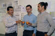 © S photographer - Three professionals celebrating success with drinks in a modern office environment, showcasing teamwork.