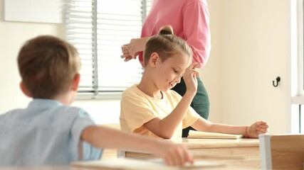 Poster - Beautiful teacher explaining test while caucasian boy doing classwork and listening explanation. Cute child looking at teacher while taking a notes or writing answer in paper at classroom. Pedagogy.