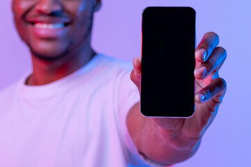 Aufkleber - Cheerful African American Guy Showing Black Smartphone Screen With Copy Space For Your App Design, Recommending New Application, Standing In Neon Light Over Purple Studio Background, Mockup Image