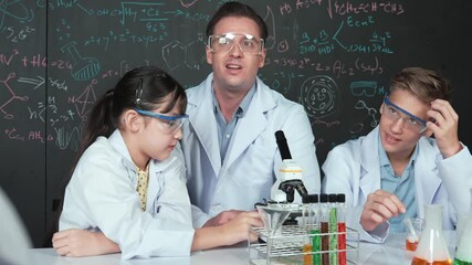 Poster - Smart teacher looking under microscope while test tube placed on table while diverse student doing experiment in front of blackboard with science theory written in creative education.. Edification