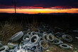 © kovop58 - Discarded tires pollute a snowy landscape, as a vivid winter sunrise highlights environmental neglect