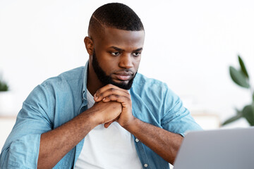 Poster - Portrait Of Thoughtful Black Freelancer Guy Sitting At Desk And Looking At Laptop Screen, Pensive African Man Thinking About Business Ideas While Working On Computer At Home Office, Free Space