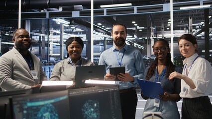 Poster - Smiling engineering team in server room reviewing infrastructure diagnostics on devices. IT professionals in data center analyzing performance data to maintain system integrity and uptime, camera A