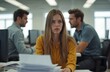 © miss irine - Young woman with long, straight hair appears distressed in office setting. Colleagues engage in heated interaction nearby. Expressive emotion of anxiety, frustration, conflict in workplace, body