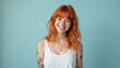 © miss irine - Cheerful young woman with ginger hair smiles wearing tank top. Female person with tattoo in studio, 20s. Happy lady with red hair, freckles poses for photo. Positive lifestyle.