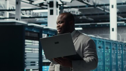 Poster - Server room worker auditing systems for vulnerabilities using software on laptop. Engineer walking in data center doing backups and recovery protocols using notebook, camera B
