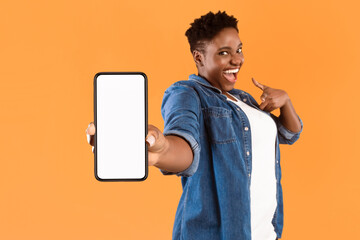 Poster - Mobile Application Ad. Excited African Woman Showing Phone Empty Screen Recommending App Standing Over Yellow Studio Background, Smiling To Camera. Cellphone Display Mockup, Check This Apps