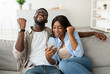 © Prostock-studio - Yeah. Emotional excited black couple celebrating online win, great deal or business success, holding using smart phone, shaking clenched fists, looking at screen, guy in glasses and braces screaming