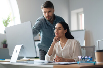 Poster - Young female trainee working on computer together with her business mentor at modern company office. New team member on probation communicating to experienced male colleague