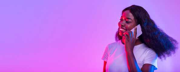 Poster - Smiling young African American woman having conversation on cellphone in neon light, banner design with copy space. Beautiful black lady talking with client or friend on smartphone