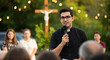 © Anna - Young priest speaking at outdoor evening church gathering with cross and string lights