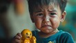 © Artsaba Family - Close up of a crying toddler boy with tears on his face, holding a broken yellow toy, expressing sadness and frustration