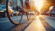 © Mariya - Close-up of a bicycle wheel and pedal in motion on a city street at sunset with blurred cars and warm glowing light creating a dynamic and energetic urban scene