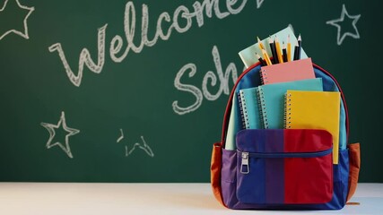 Poster - School backpack full of notebooks, pens, and pencils sits on a table against a green chalkboard with welcome school written on it, stars and other drawings