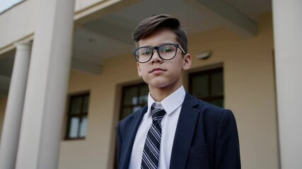 Aufkleber - Young student wearing suit, tie, glasses standing confidently before columned school building, representing academic preparedness and professional demeanor