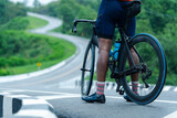 A cyclist with a road bike pauses on a winding road surrounded by greenery, ready for a ride or rest.