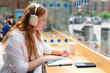 © Iryna - Young woman with headphones writes in notebook at urban cafe during daylight hours surrounded by city life