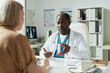 © pressmaster - Middle aged Black male doctor explaining medication to middle aged Caucasian woman patient during diabetes consultation in medical office, prescription bottle visible on desk