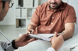 © pressmaster - Middle aged Caucasian man consulting doctor in medical office, discussing diabetes management while holding clipboard and pen, hands and partial faces visible, healthcare concept