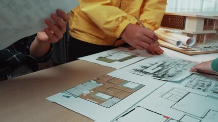 Poster - Two individuals engage in a collaborative design process, reviewing detailed architectural blueprints and sketches on a wooden table in a stylish workspace. SACTR