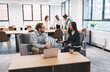 © BullRun - Caucasian man and Asian woman seated in open-plan office lounge discussing project strategy, with laptop and coffee mug on table, portraying teamwork and digital-era leadership exchange