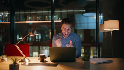 Poster - Excited late worker rejoicing online win looking laptop screen at dark workplace