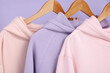 © Pixel-Shot - Hangers with stylish hoodies on lilac background, closeup