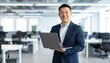 © 순단 강 - A Korean man in a suit holding a laptop computer to the right, with luxury office furniture in the blurred background