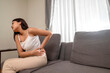 © Leo Lintang - Indonesian southeast asian woman suffering from back pain while sitting on the living room couch at home. Healthcare concept