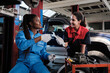 © tigercat_lpg - Two cheerful diverse female mechanic workers, Latin and Black coworkers fix automotive wheels, maintain car suspensions in garage, technician engineering service jobs in vehicle transport industry.