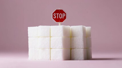 Poster - White sugar cubes stacked neatly on a pink background, topped with a miniature stop sign, symbolizing the need for sugar reduction and promoting a healthy lifestyle