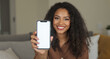 © Asad - Smiling woman holding a smartphone with a blank screen indoors at home
