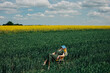 © VISTA by Westend61 - Woman relaxing on a yellow folding chair in a field of green wheat and yellow rapeseed, reading a book under a cloudy sky