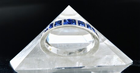 Poster - Silver ring with blue stones rests upon clear quartz pyramid. Minimalist jewelry presentation, clean background, studio lighting.