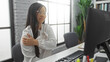 © Krakenimages.com - Woman holding arm in pain at modern office with computer, glasses, and plants, portraying stress or discomfort during work in a bright, professional indoor setting.