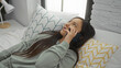 © Krakenimages.com - Woman relaxing on bed in modern bedroom while talking on phone, wearing cozy clothes, surrounded by patterned pillows and soft light, creating a calm, intimate indoor atmosphere.