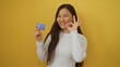 © Krakenimages.com - Smiling woman holding credit card in front of yellow background making okay gesture smiling confidently